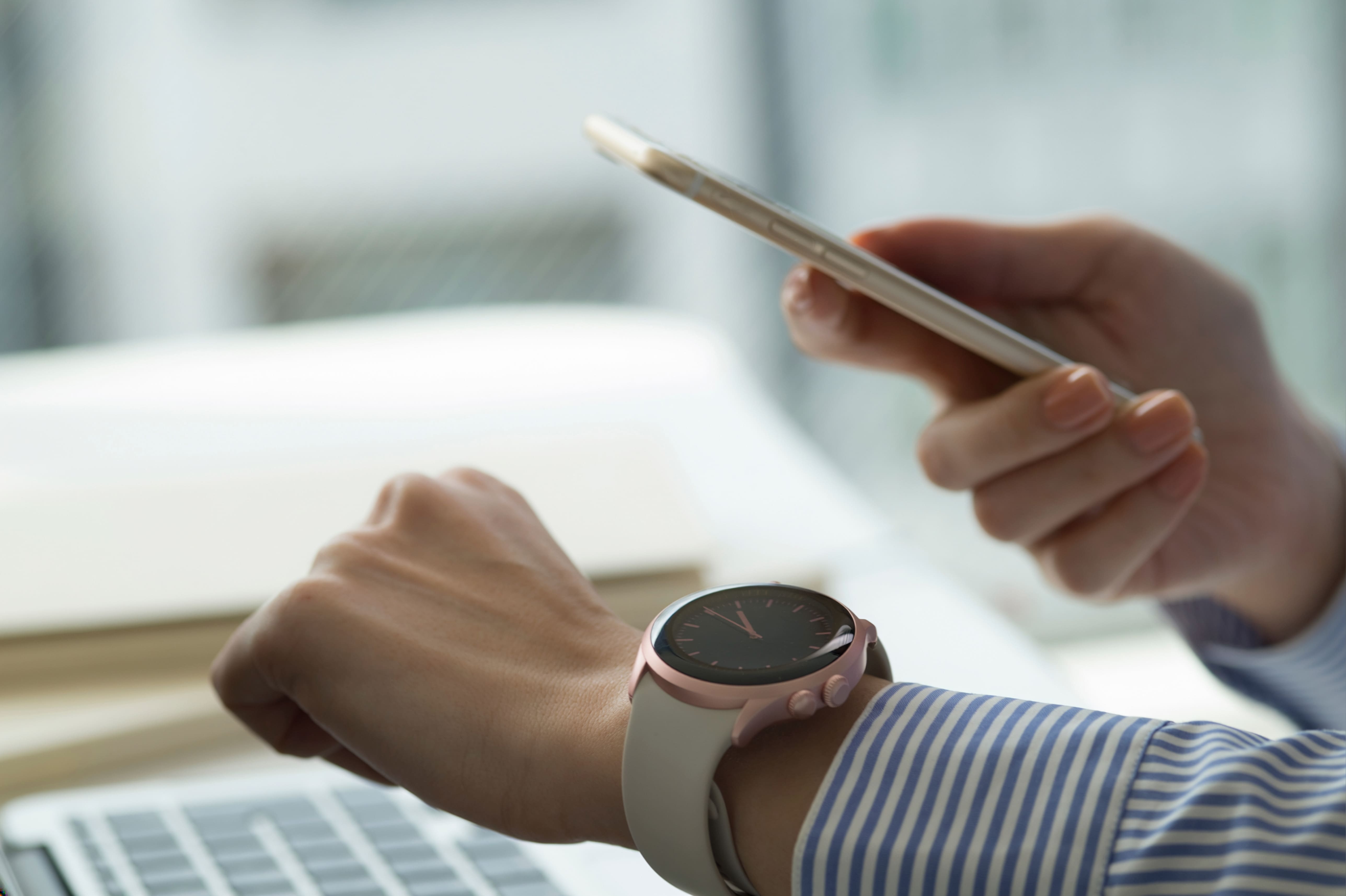 スマートフォンを片手に、身につけたスマートウォッチを確認する人